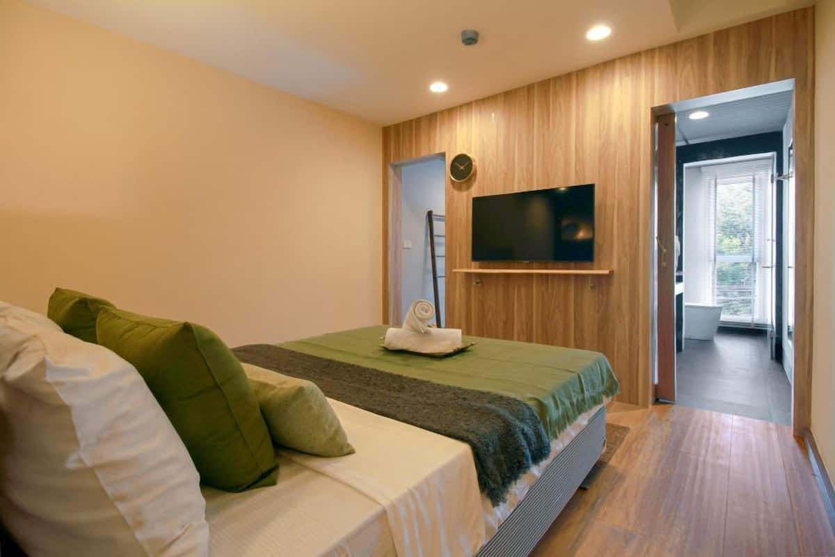 A bedroom with a bed, pillows, a TV mounted on the wall, and a wooden panel design.