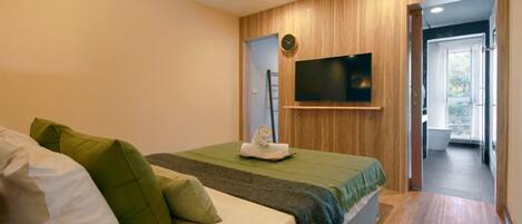 Un dormitorio con cama, almohadas, un televisor montado en la pared y un diseño de paneles de madera.