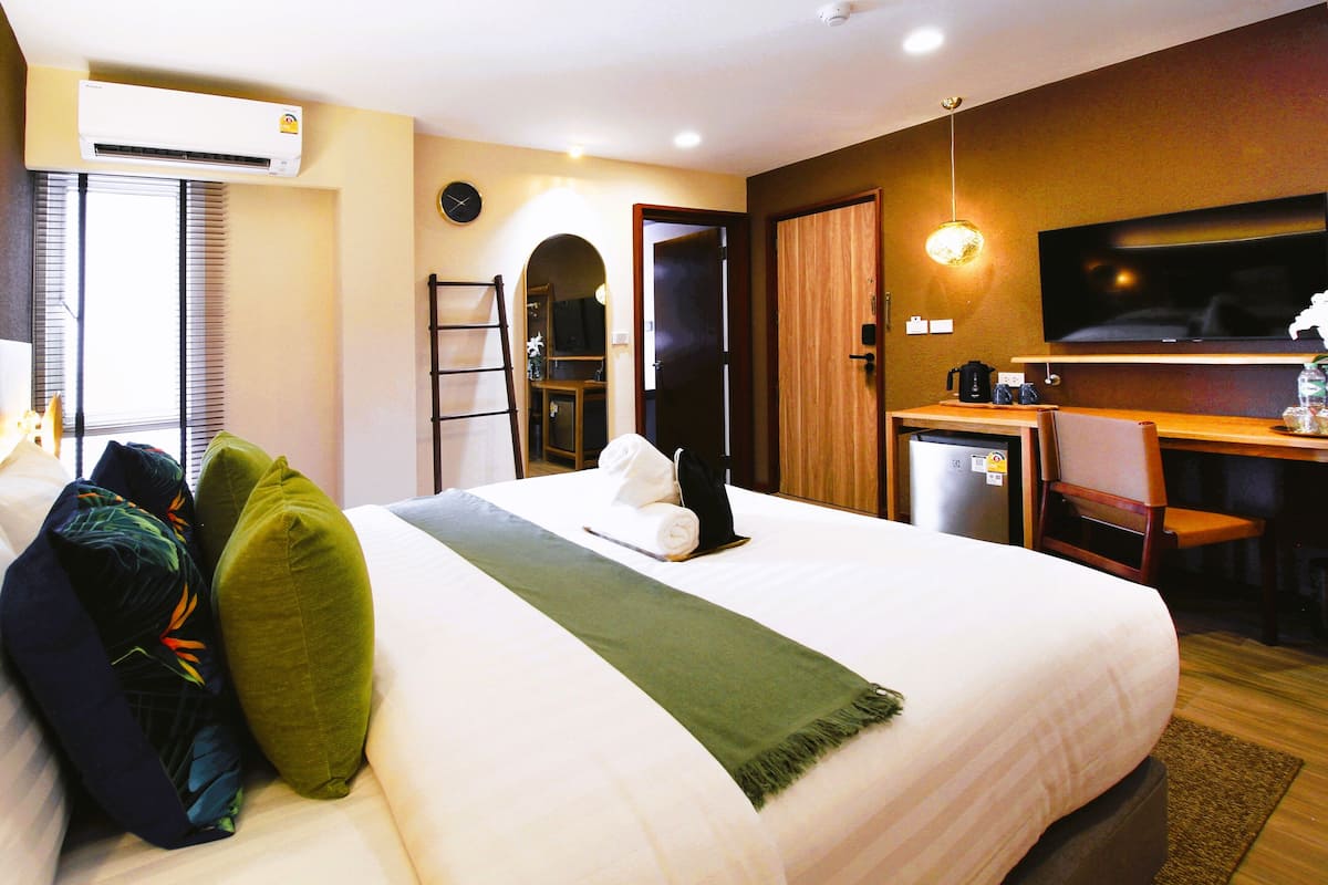 A hotel room with a bed, a desk, a TV, and an air conditioning unit.