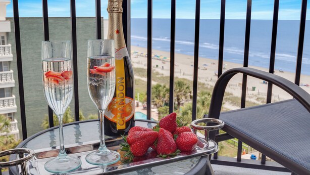 Un balcon avec vue sur la plage, une bouteille de champagne Chandon, deux verres et un plateau de fraises.