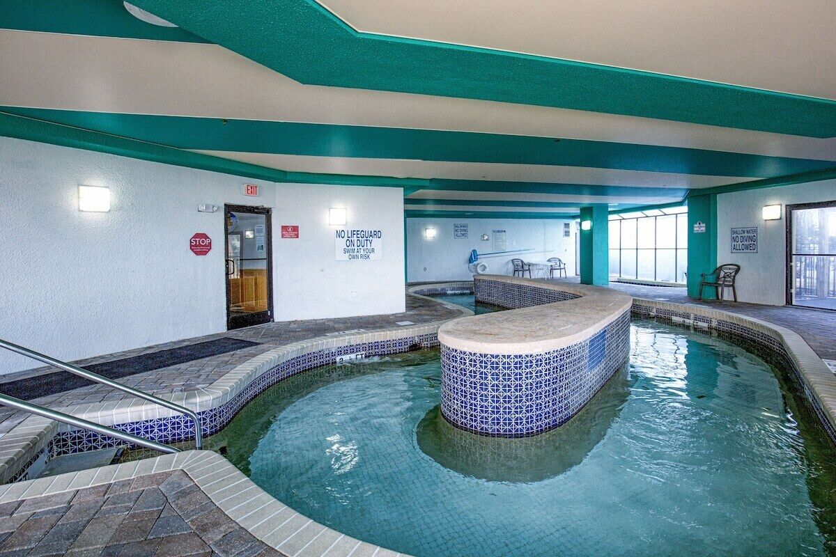 An indoor swimming pool with tiled walls and a central fountain, a stop sign, and a lifeguard duty sign.