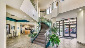 A spacious lobby with a central staircase, a reception area, and a view of the outside.