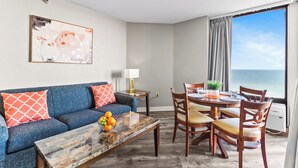 A living room with a sofa, coffee table, and dining area with chairs and a table. - Grand Oceanfront 1Br Suite! Dogs OK! (Myrtle Beach)