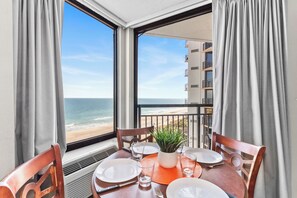 A dining table with chairs, a potted plant, and a view of the beach and ocean through large windows. - Grand Oceanfront 1Br Suite! Dogs OK! (Myrtle Beach)