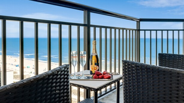 A balcony with a table set for two, featuring a bottle of champagne, two glasses, and strawberries. - Inviting 1BR Oceanview Suite/Dogs OK (Myrtle Beach)