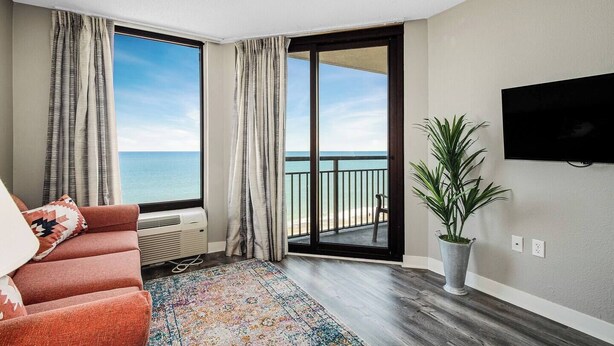 A balcony with a view of the sea, a sofa, a TV, and a potted plant. - Paradise Awaits @ Oceanfront Suite/Dogs OK! (Myrtle Beach)