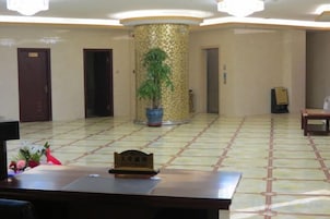 Un hall de hotel con mostrador de recepción, una planta en maceta y suelo de baldosas.