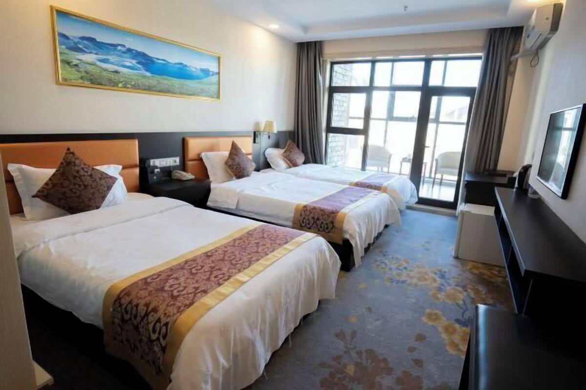 A hotel room with two beds, a desk, a TV, and a large window.