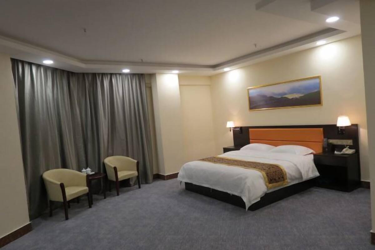 A hotel room with a bed, two chairs, a nightstand, a lamp, and a painting on the wall.