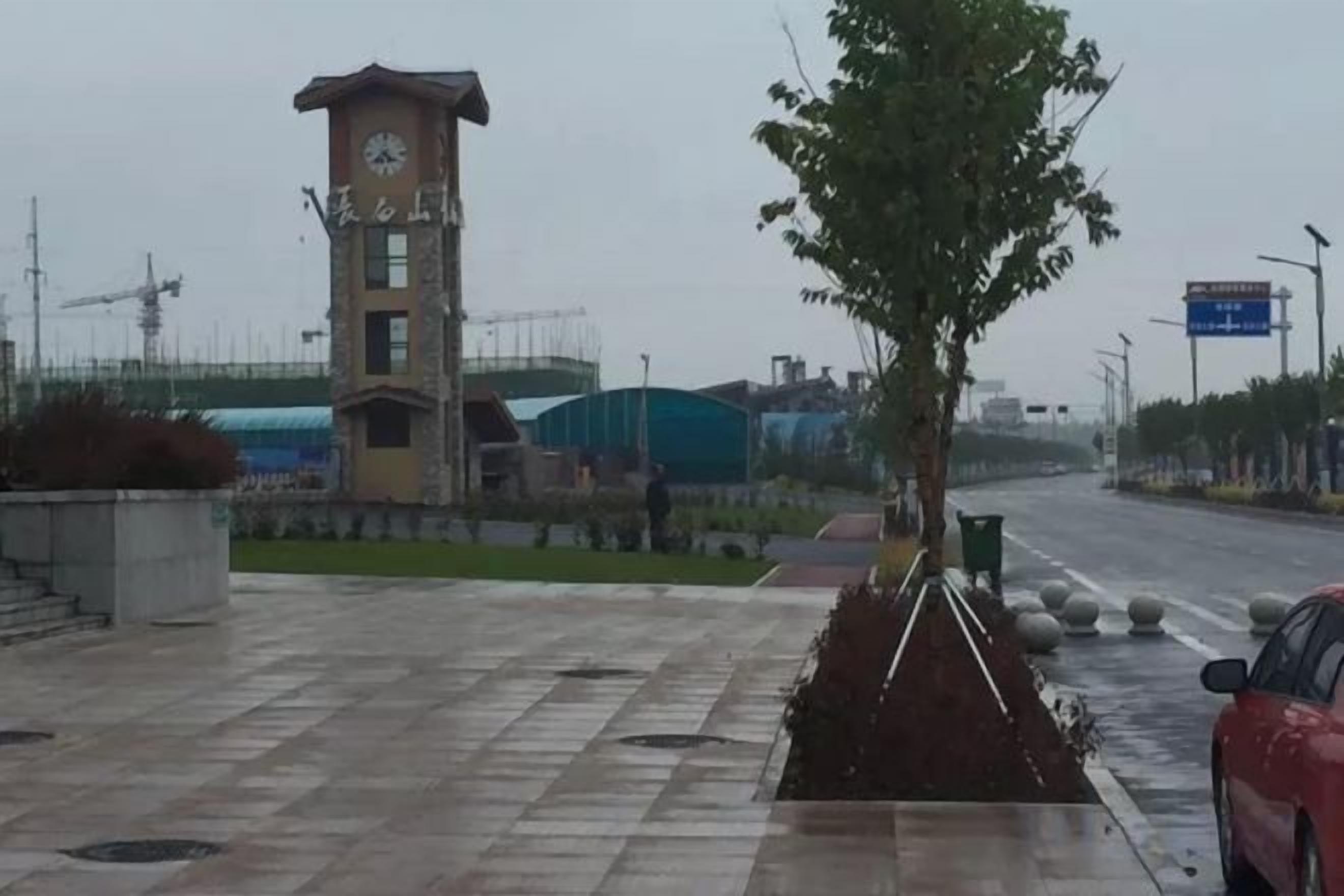 A clock tower, a paved walkway, and a road with a red car.