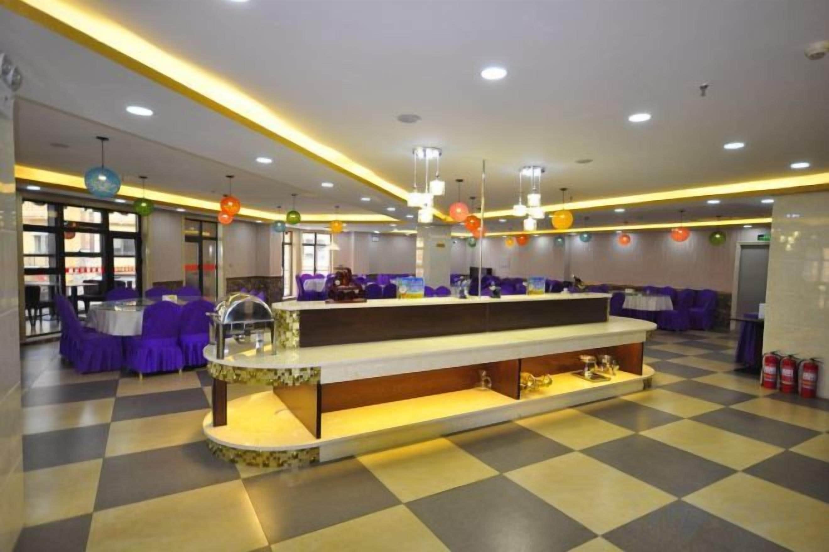 A hotel lobby with a checkered floor, a reception desk, purple seating, and pendant lighting.