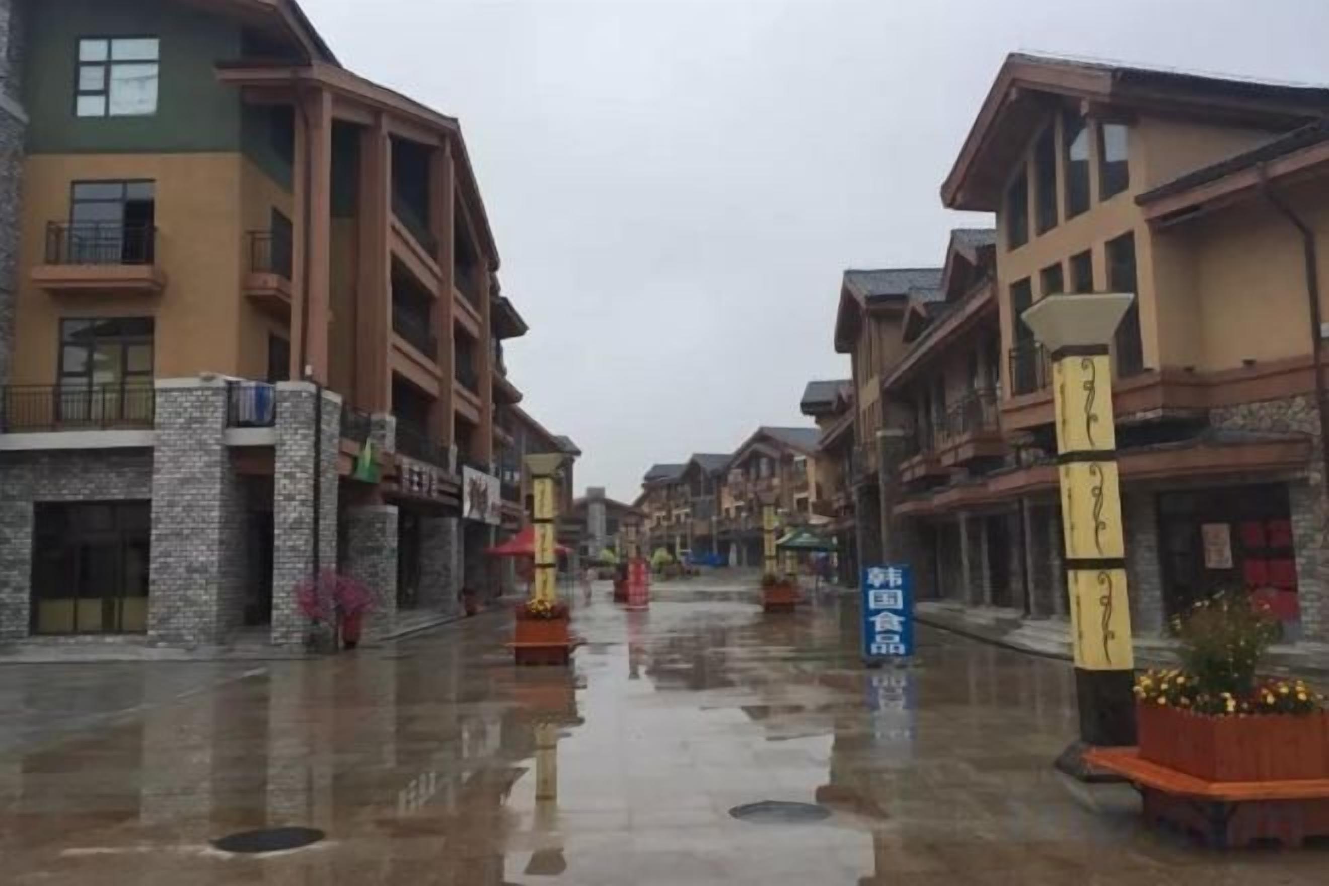 A wet street with buildings on either side, a clear sky, and a blue sign with white text.
