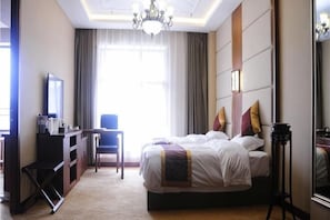 A hotel room with a bed, a desk, a chair, a television, and a large window with curtains.
