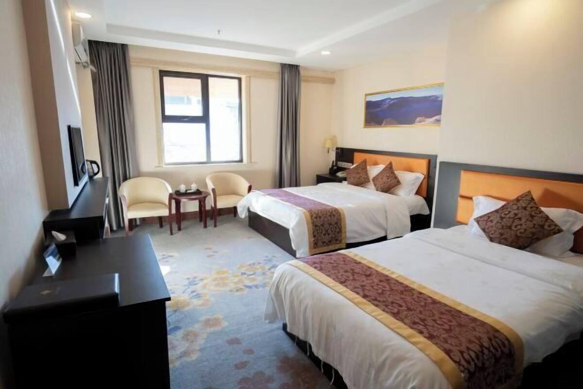A hotel room with two beds, a desk, a chair, and a large window.