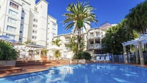 Ein Swimmingpool, umgeben von Palmen und ein mehrstöckiges Gebäude mit Balkonen.