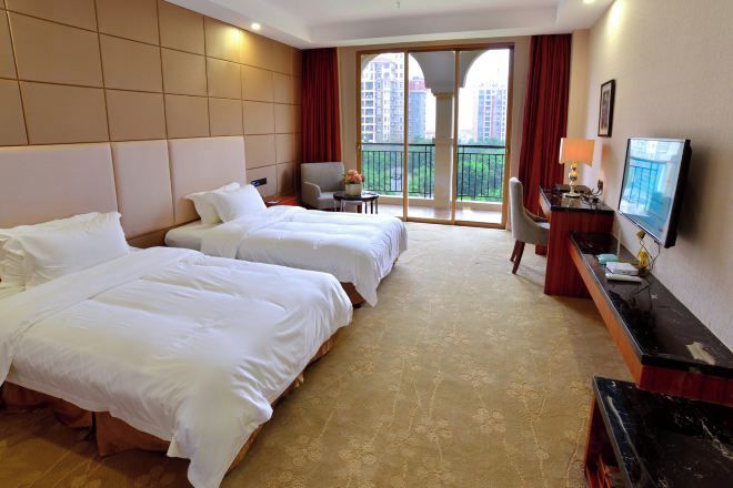 Habitación de hotel con dos camas, un escritorio, un televisor y un balcón con vistas a edificios.