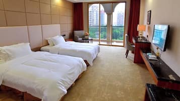 Habitación de hotel con dos camas, un escritorio, un televisor y un balcón con vistas a edificios.