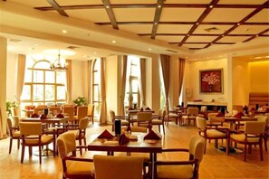 Un vaste espace dédié à la salle à manger, avec de nombreuses tables et chaises, de grandes fenêtres et un lustre.