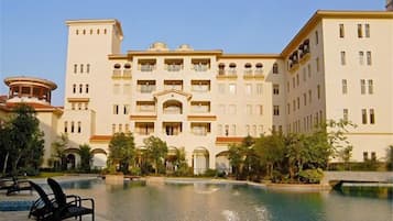 A hotel with a swimming pool, multiple balconies, and a courtyard with palm trees.
