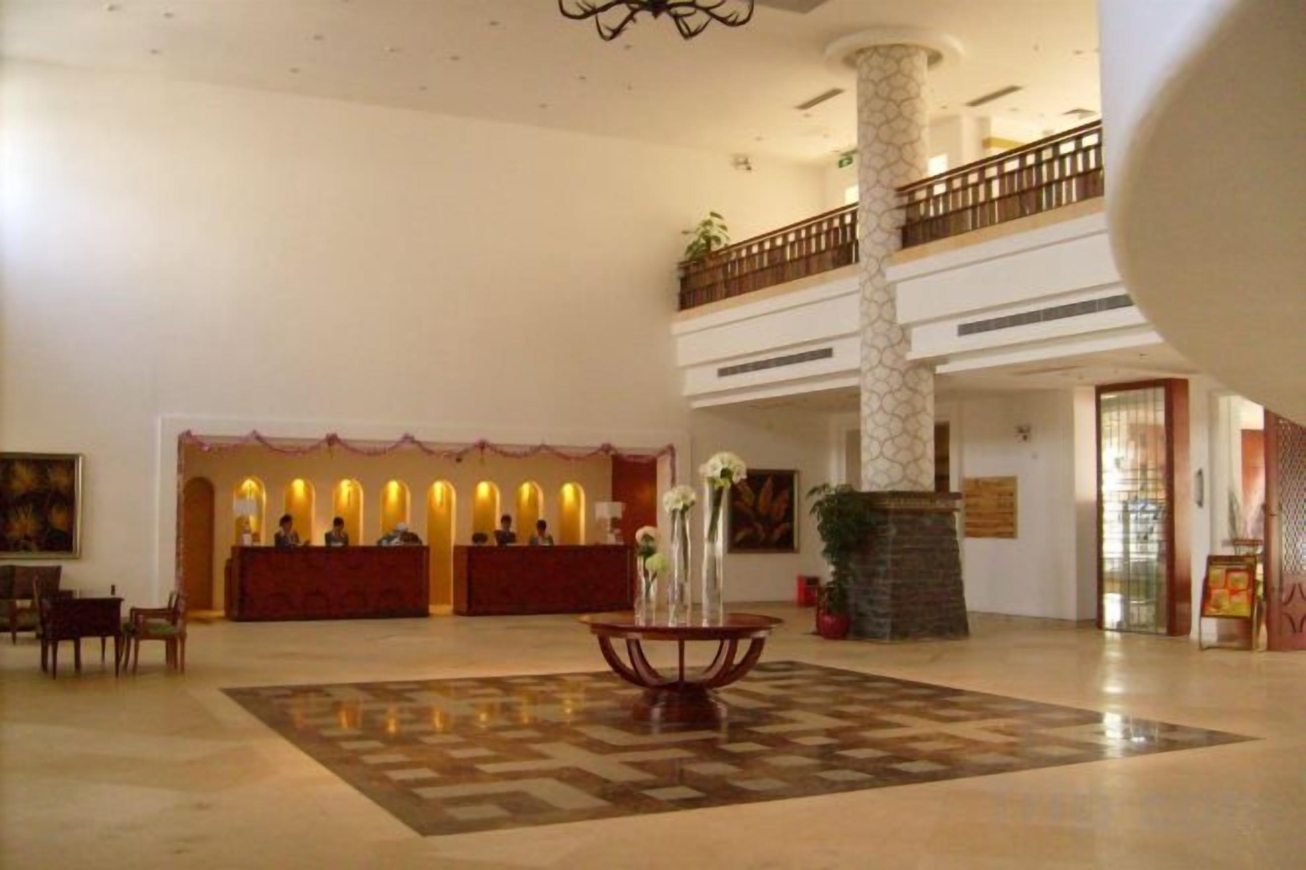 A hotel lobby with a reception desk, a check-in counter, a large decorative vase, and a high-ceilinged atrium.