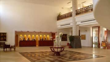 A hotel lobby with a reception desk, a check-in counter, a large decorative vase, and a high-ceilinged atrium.