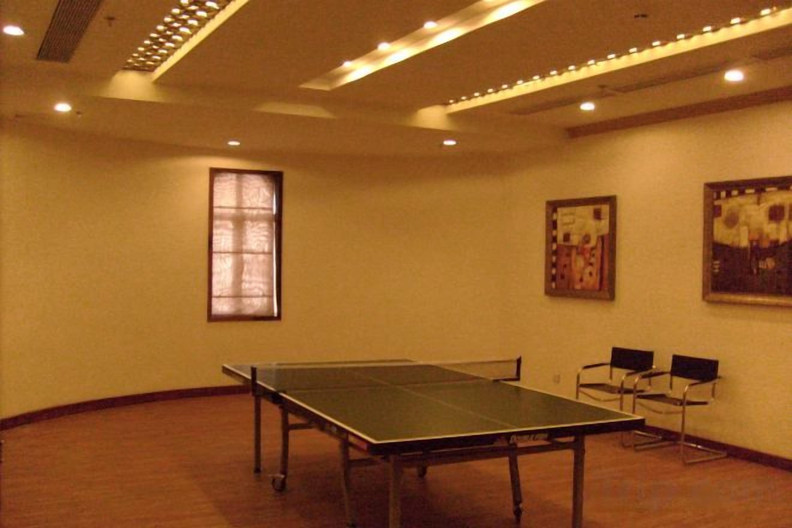 Un salón de conferencias con mesa de ping pong, sillas, una ventana y decoración en la pared.