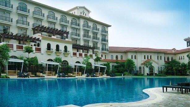 Un hotel con piscina, mobiliario exterior y un edificio grande con varios balcones.