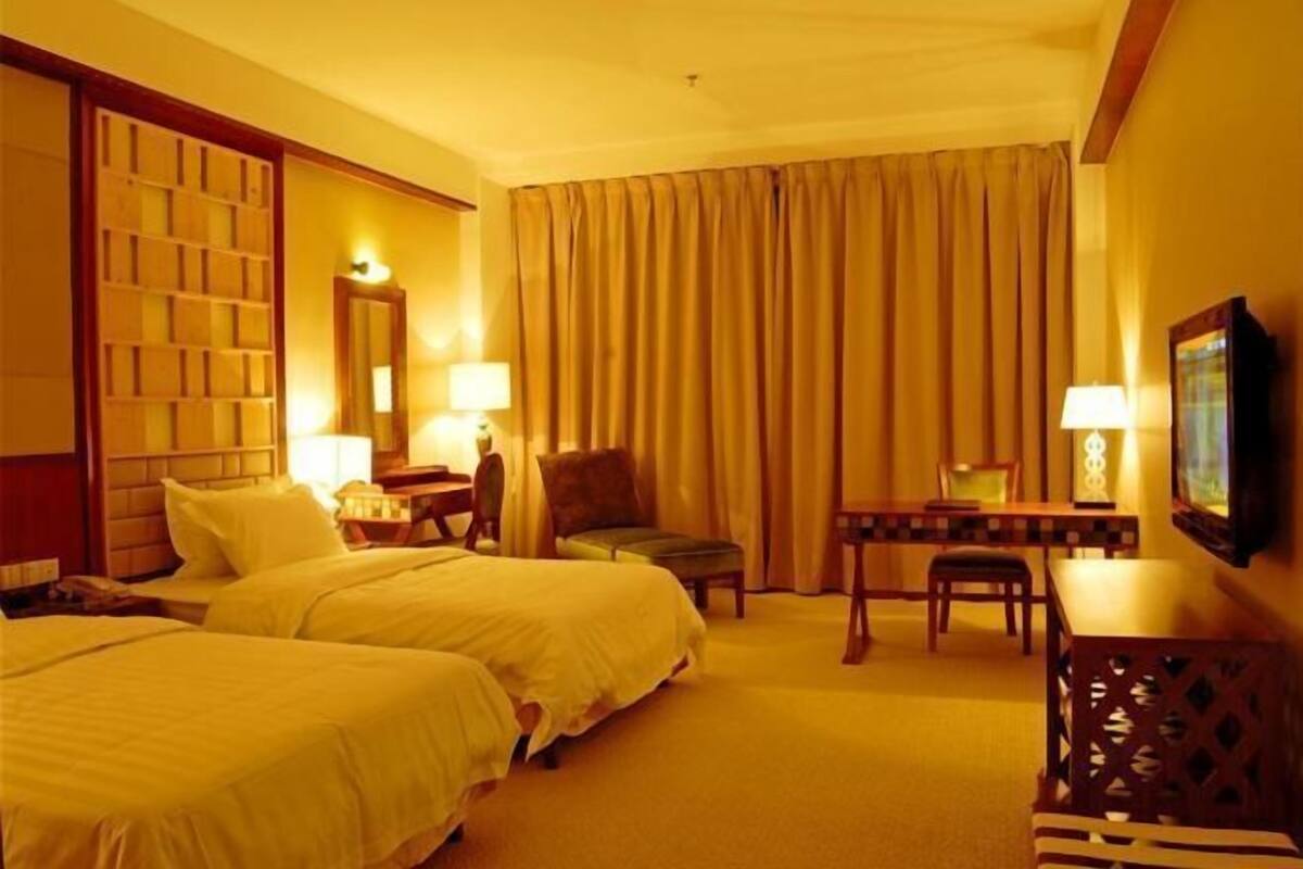 Habitació d'hotel amb dos llits, una taula de treball, una cadira, televisió i una finestra gran amb cortines.