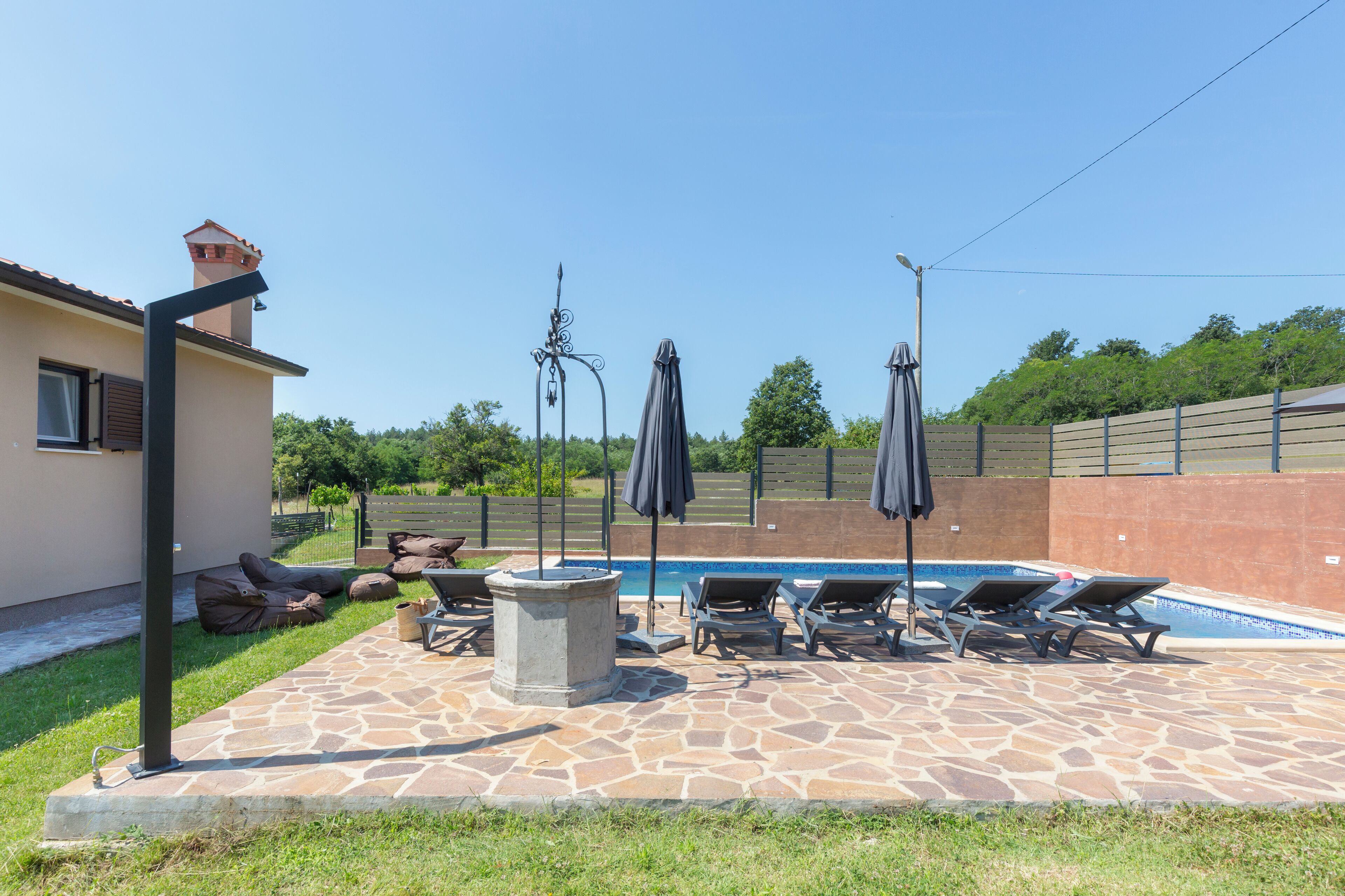 Un espace piscine avec des chaises longues et des parasols, une terrasse en pierre et une vue sur le paysage environnant.