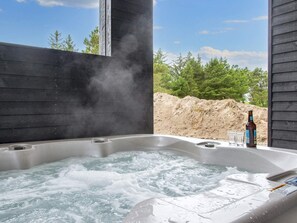 Un bain à remous avec une bouteille et des verres, entouré d’une structure en bois et d’arbres.