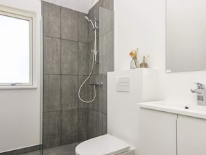A modern bathroom with a shower, toilet, sink, and a mirror. - 5 Star Holiday Home in Romo (Rømø)