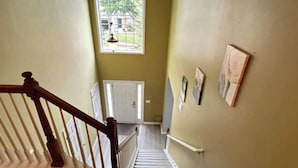 Eine Treppe mit Holzhandläufen und einem weißen Geländer, die zu einem Raum mit einer weißen Tür und einem Fenster mit Blick auf Grünanlagen führt.