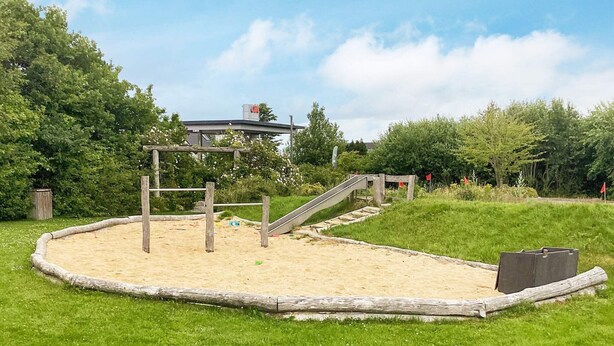 Une aire de jeux avec un bac à sable, des structures d’escalade en bois et un toboggan.