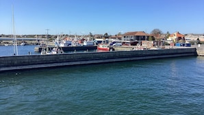Un port de plaisance avec des bateaux amarrés, une digue en béton et des immeubles résidentiels en arrière-plan.