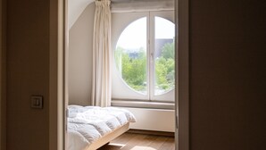 Un dormitorio con cama, ventana redonda y vistas al verdor exterior.
