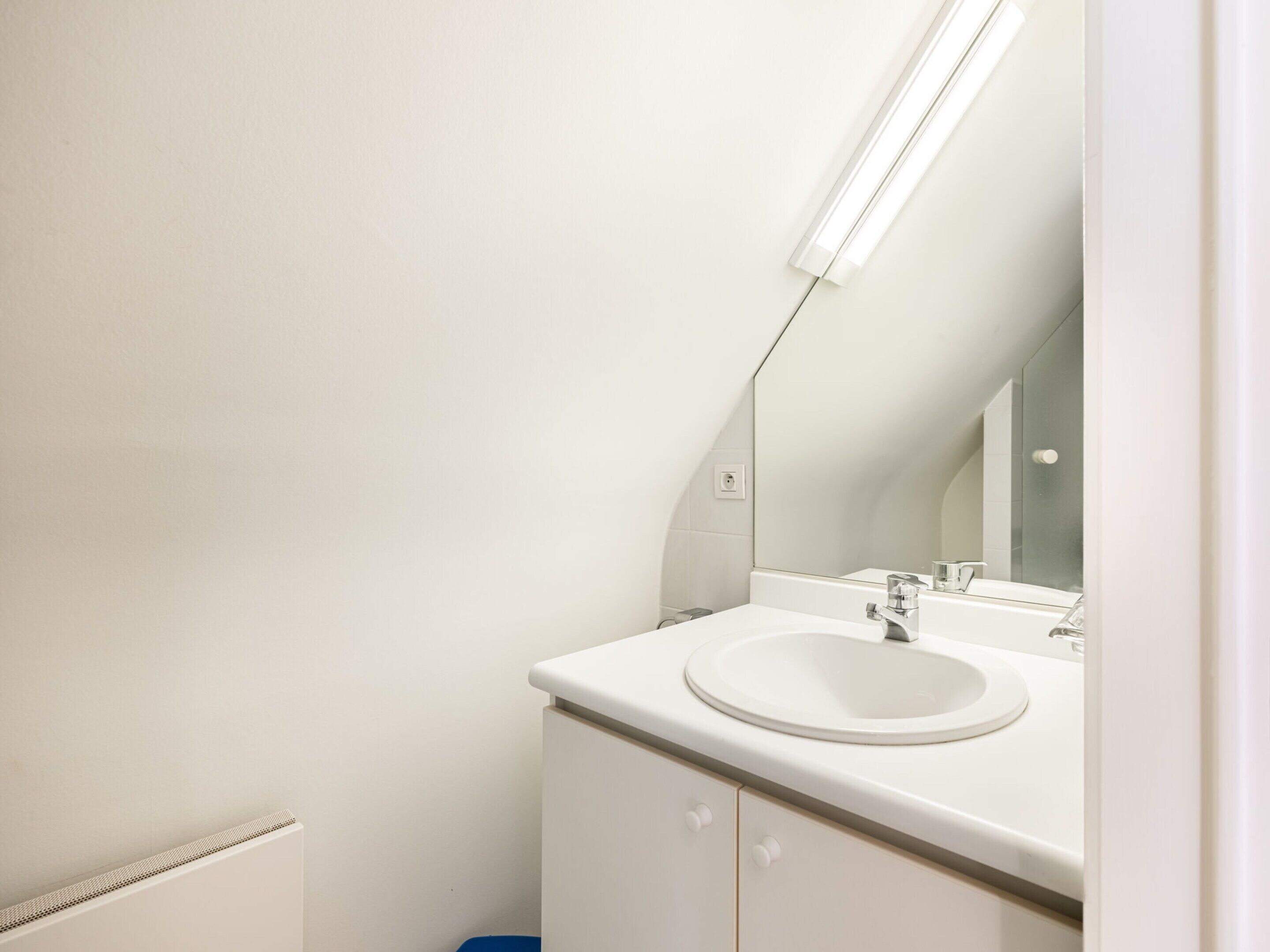 A modern bathroom with a white sink, mirror, and a light fixture above the mirror.