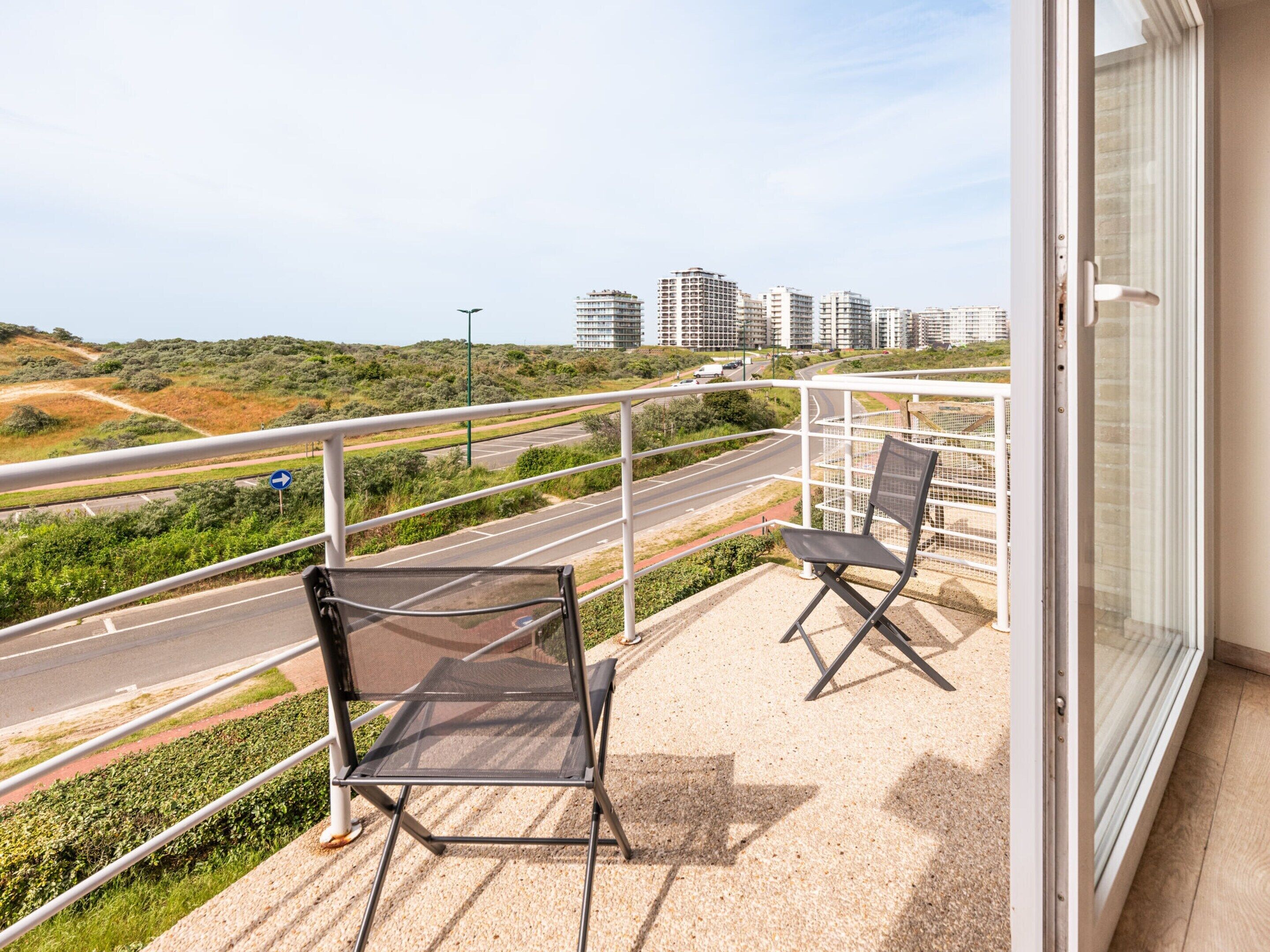 Un balcon avec deux chaises, une vue sur une route et, au loin, des immeubles de grande hauteur.