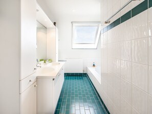 Een moderne badkamer met witte wanden, een dakraam, een badkuip en een betegelde vloer.