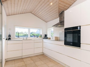 A modern kitchen with white cabinets, a black oven, and a window with a view of greenery. - 5 Star Holiday Home in Lokken (Lokken)