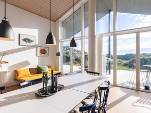A modern interior with a large dining table, blue chairs, a yellow sofa, and large windows offering a view of the outdoors.