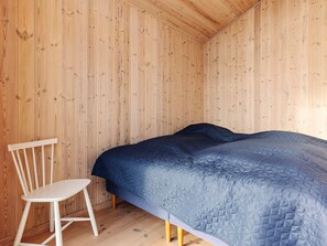 A room with wooden walls, a bed with a quilted cover, and a white chair.