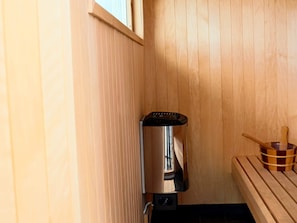 A sauna room with a wooden bench, a sauna heater, and a wooden bucket.