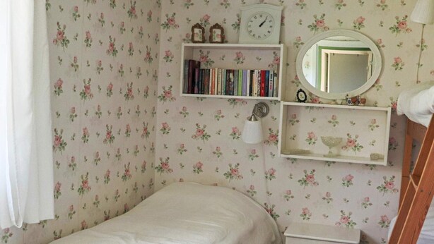 A bedroom with a single bed, a bedside table, a small shelf with books, a wall clock, and a mirror. - 7 Person Holiday Home in Skummeslovsstrand (Skummesloevsstrand)