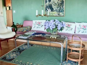 A living room with a sofa, a glass coffee table, a wicker chair, and a patterned rug.