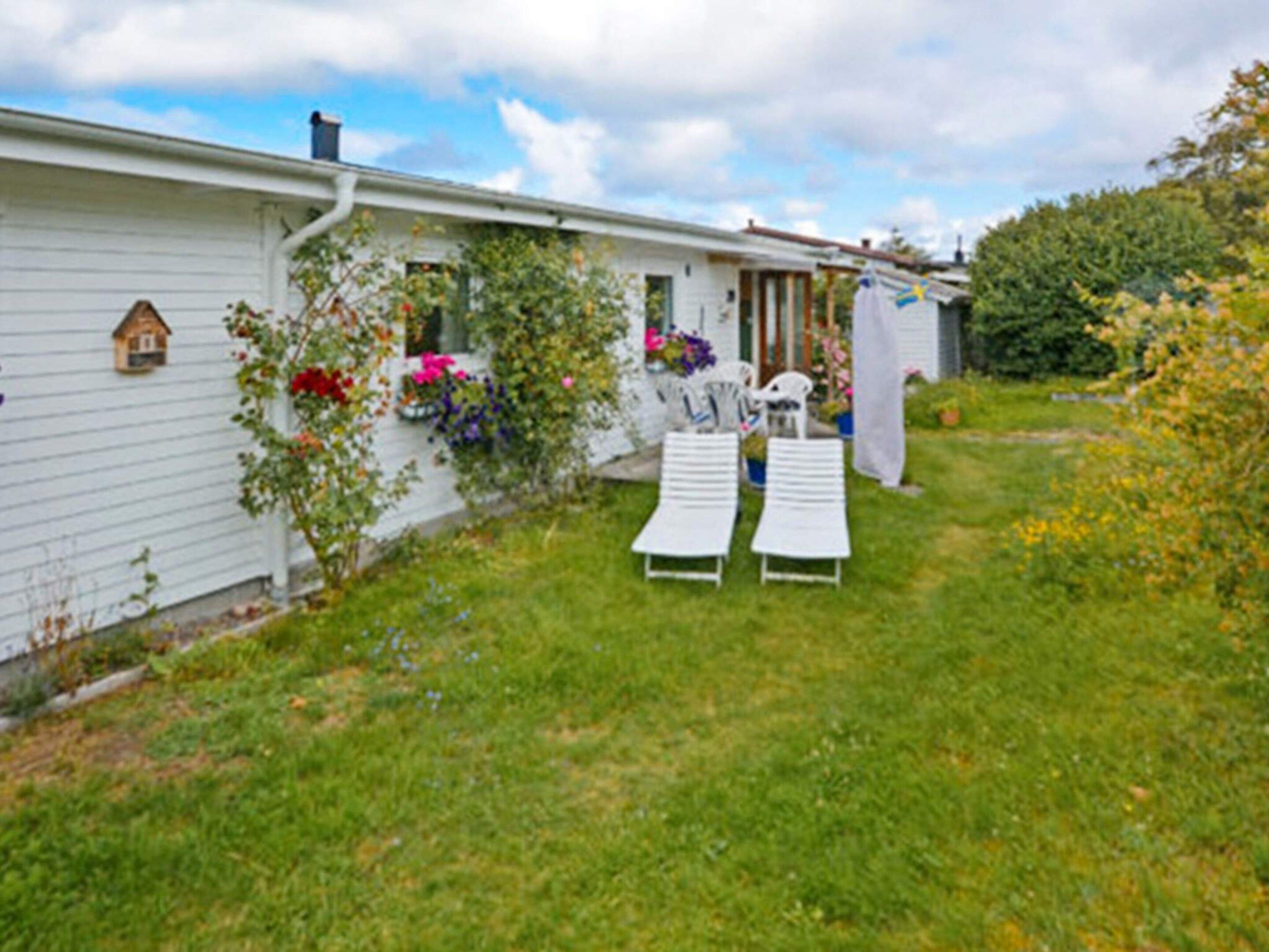 Ett vitt hus med en liten trädgård, två vita solstolar och en flagga.