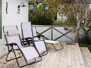Una terraza de madera con dos sillas reclinables y una pequeña mesa.