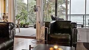 A room with a view of the water, a black leather chair, a table with a bowl, candles, and a remote control. - 5 Star Holiday Home in Haro (Harö)