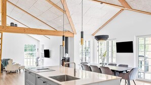 Une cuisine moderne dotée d’un îlot central, de poutres en bois et d’un coin repas avec une grande fenêtre.