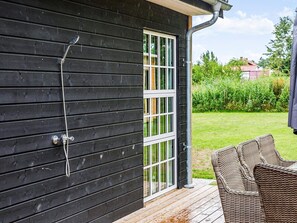 A wooden exterior with a sliding glass door, a metal hose, and wicker furniture on a wooden deck. - 5 Star Holiday Home in Vaeggerlose (Vaeggerlose)