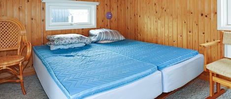 A wooden-paneled room with a bed, a window, and a chair.